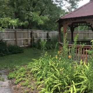 A tranquil garden featuring a wooden gazebo surrounded by lush greenery and enclosed by a fence.
