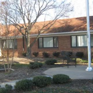 A brick building surrounded by trees and shrubs with a flagpole in the foreground.