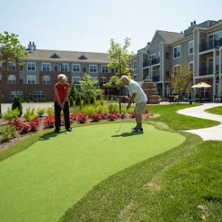 Seniors enjoying a game of mini golf on a sunny day in a beautifully landscaped residential community.
