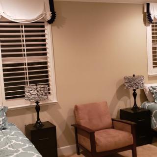 A cozy bedroom with a chair, twin beds, and lamps beside shuttered windows.