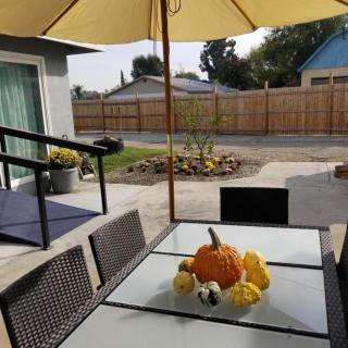 An outdoor patio with a table set under an umbrella, featuring autumn decorations including a pumpkin.