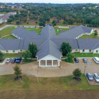 Aerial view of a large building with a parking lot and surrounding trees.