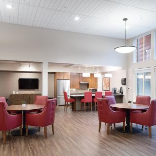 A modern dining and kitchen area with red chairs and wood flooring.