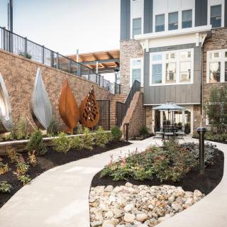 A modern garden with unique sculptures and a winding pathway alongside a contemporary building.