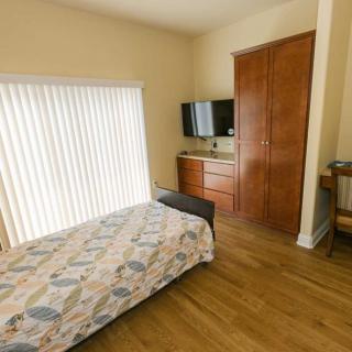 A cozy bedroom with a single bed, TV, dresser, and wooden flooring.