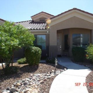A single-story house with a stucco exterior and tile roof, surrounded by desert landscaping.