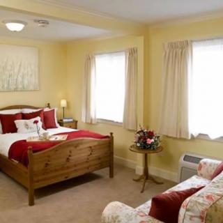 A cozy bedroom with a wooden bed, warm lighting, and soft yellow walls, featuring two windows with curtains.