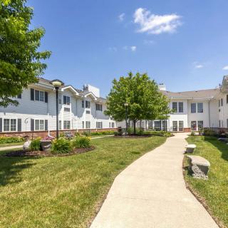 A sunny day with a view of a building, surrounded by trees and a well-maintained lawn, alongside a winding pathway.