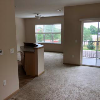 A spacious apartment living area with a view of the kitchen and balcony.