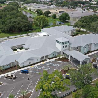 Aerial view of a large building with a parking lot surrounded by trees and roads in a residential area.