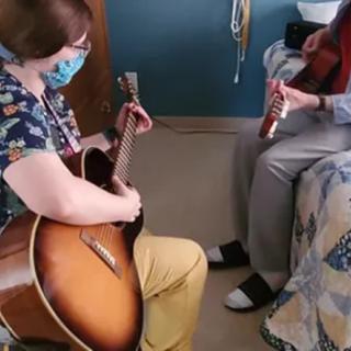 Two people playing music together indoors, one on a guitar and the other on a flute.