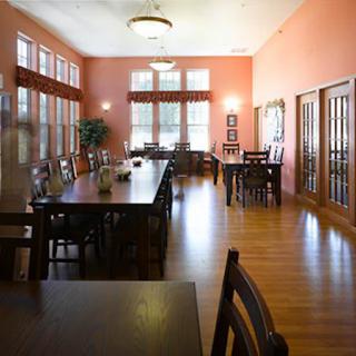 A spacious dining room with large windows, wooden tables and chairs, and a hardwood floor.