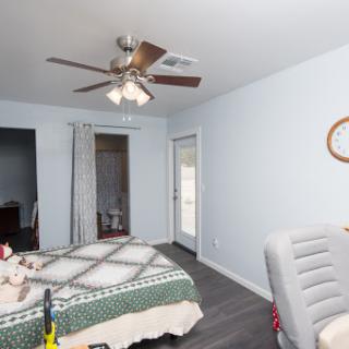 A cozy and well-lit bedroom featuring a ceiling fan, a bed with an intricate quilt, and modern decor.