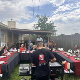 A group of people enjoying an outdoor BBQ gathering in a backyard setting.