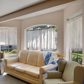 A cozy living room filled with natural light, featuring comfortable seating and large windows with sheer curtains.