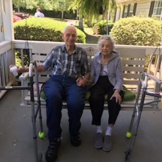 An elderly couple holding hands while sitting on a porch swing.