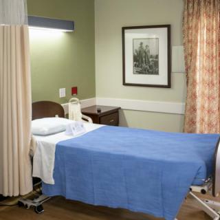 A clean and organized hospital room with a bed covered in a blue blanket, surrounded by curtains.