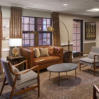 A cozy living room with modern furnishings, including a leather sofa, stylish chairs, coffee table, and elegant lighting.