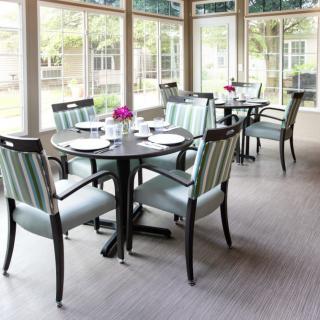 A bright and airy dining area with neatly arranged tables and chairs, accented by natural daylight filtering through large windows.