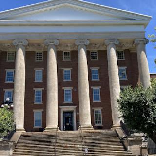 A grand brick building featuring prominent columns and a well-structured facade, inviting visitors up the steps to its entrance.