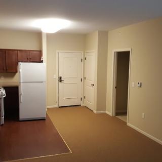 A spacious kitchen area in an apartment, showcasing a refrigerator and multiple doorways.