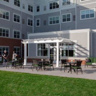 An outdoor patio area with tables and chairs, located next to a modern building.