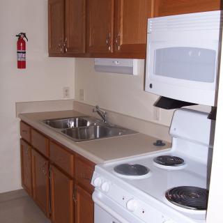 A compact kitchen with wooden cabinets, a stove, microwave, sink, and countertop.