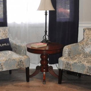 A cozy living room corner featuring two patterned chairs flanking a wooden side table with a lamp.