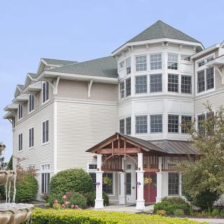 A three-story residential building with large windows and a green roof, surrounded by well-maintained greenery.