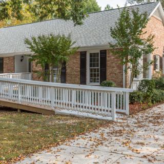 A single-story brick house with a white accessibility ramp surrounded by trees and fall leaves.