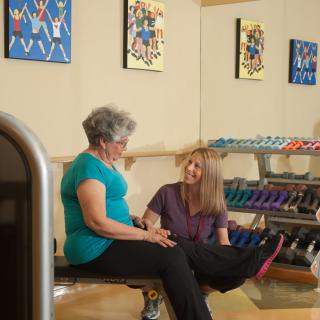 Two women engaging in a fitness session at the gym, with weights visible in the background.