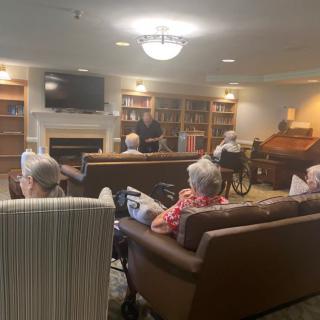 A group of elderly individuals sitting in a cozy library at a retirement home, engaging in conversation and activities.