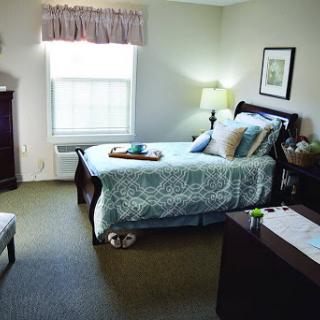 A cozy and well-lit bedroom featuring a neatly made bed and comfortable furnishings.
