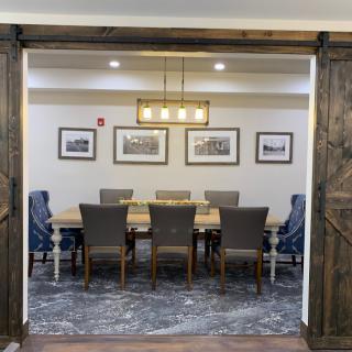 A well-decorated dining or meeting room with a large wooden table, surrounding chairs, stylish lighting, and framed artwork on the walls.