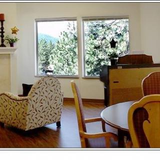 A cozy living room with a fireplace, piano, and large windows overlooking the outdoors.