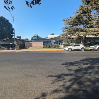 A sunny day on a quiet street featuring residential buildings and parked cars.