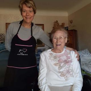 A caregiver and an elderly woman smiling together in a home setting.