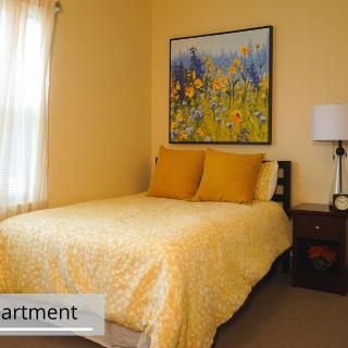 A cozy bedroom with a yellow bedspread and floral painting.