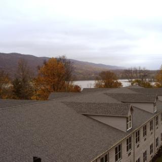 A serene view of a river surrounded by mountains and autumn foliage, with rooftops in the foreground.