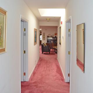 A hallway with red carpet, featuring several doors and decorated with artwork on the walls.
