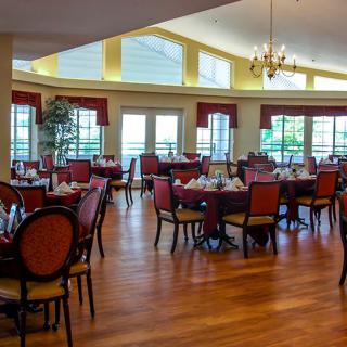 A spacious dining area with elegantly set tables and chairs, featuring large windows and a chandelier.