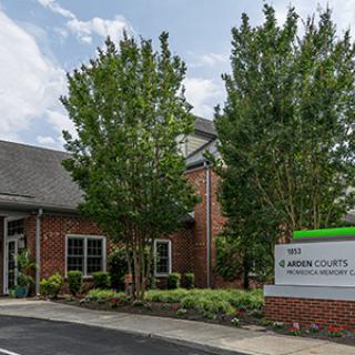 A brick office building surrounded by trees, featuring a sign at the entrance under a cloudy sky.