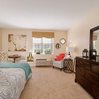 A cozy bedroom interior with a bed, dresser, chair, and various decor items.