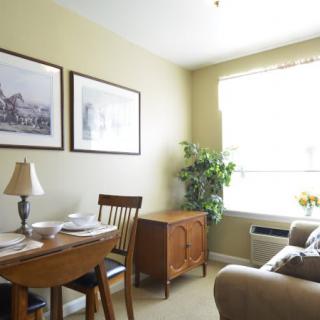 A cozy dining area with a table set, chairs, artwork on the wall, and natural light from a window.