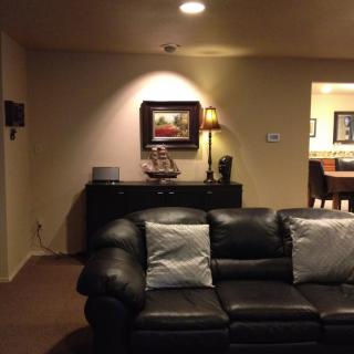 A cozy living room with a black leather couch, decorative pillows, and a well-lit artwork above a side table.