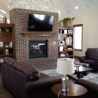 A cozy living room with a brick fireplace, featuring a mounted television and comfortable seating.