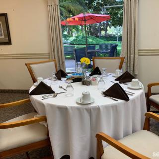 A neatly set dining table with chairs and a view of an outdoor patio through the window.