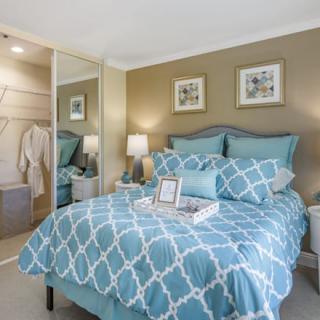 A cozy bedroom with a blue patterned bedspread, mirrored closet doors, and stylish decor.
