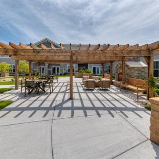 A spacious outdoor courtyard featuring a wooden pergola and patio furniture under a sunny sky.