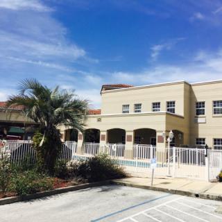 A school building with a palm tree and parking area under a clear blue sky.